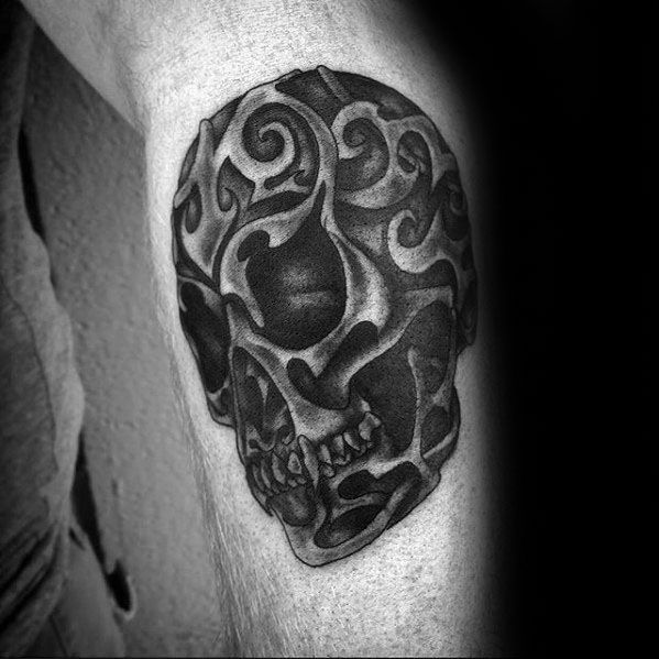 Tribal skull tattoo on upper arm with dark swirling patterns and deep shading, blending realism with abstract tribal design.