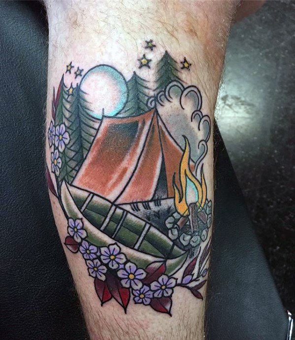 Alt text: Vibrant tattoo of a camping scene with a tent, campfire, canoe, and flowers, set against a forest backdrop under a starry sky.