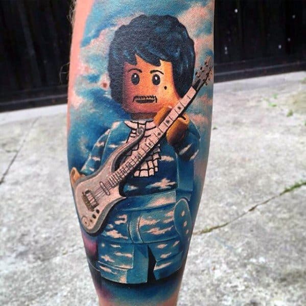 Vibrant tattoo of a Lego minifigure dressed in a blue outfit playing an electric guitar, set against a cloudy sky background.