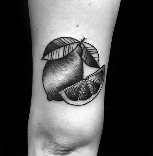 Black and grey tattoo of a whole lemon with bold leaves and a detailed lemon wedge, shaded for a realistic, textured look.