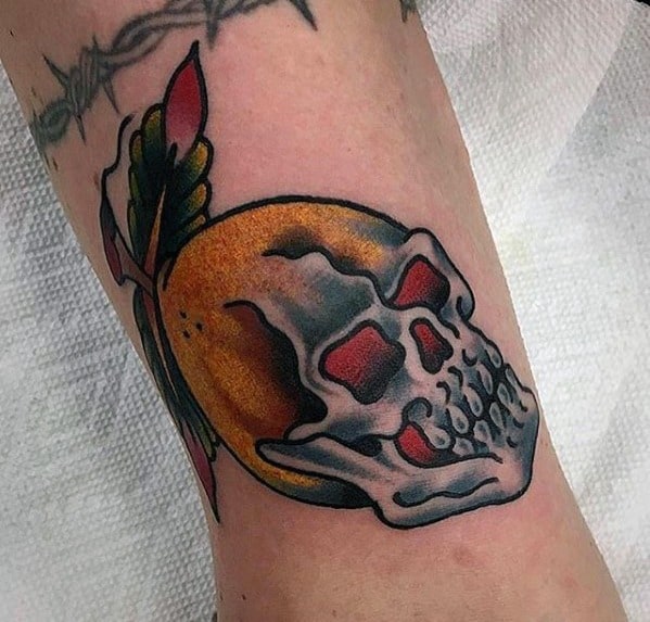 Bold neo-traditional tattoo of a lemon with a skull overlay, red eyes, and dark leaves, blending fruit and gothic elements.