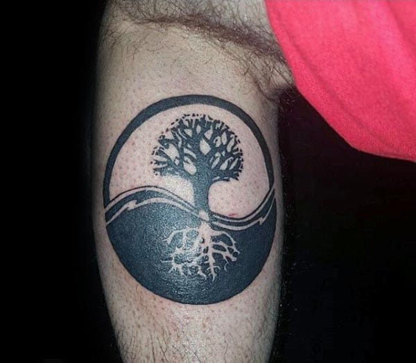 Tattoo of a tree of life with visible roots inside a circular design on an arm