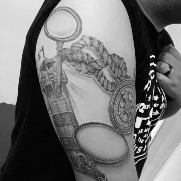 Tattoo featuring a magnifying glass, compass, rope, and lighthouse, creating a nautical-themed design with intricate shading and depth.