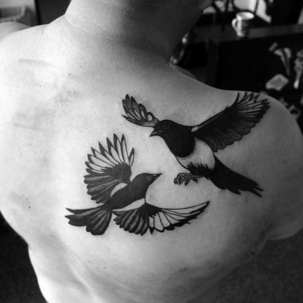 Black and gray back tattoo featuring two magpies in flight, wings spread wide, symbolizing freedom, balance, and movement with bold contrast.