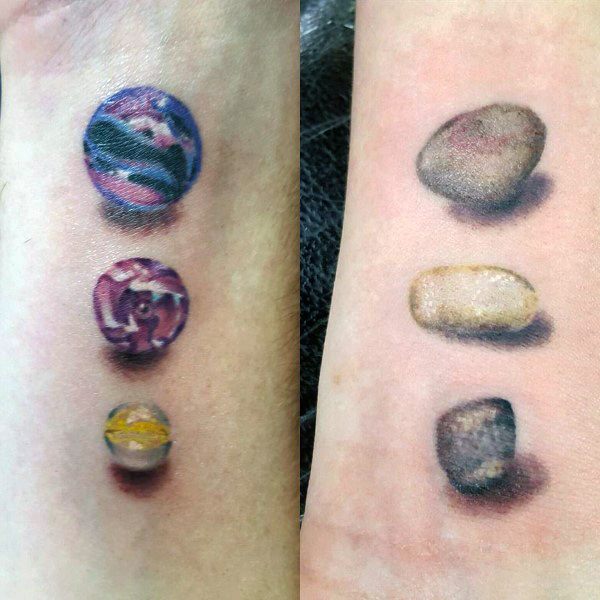 Realistic forearm tattoos featuring marbles on one side and pebbles on the other, with detailed shading for a striking 3D effect.