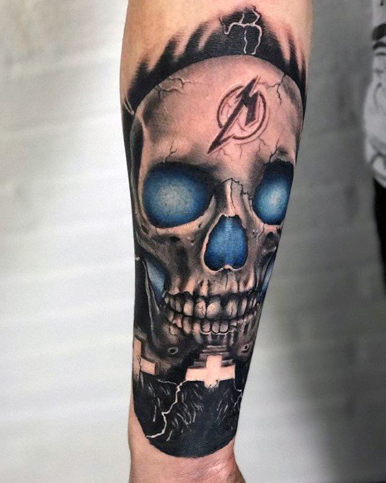 Colorful forearm tattoo of a skull with glowing blue eyes, Metallica logo on the forehead, and white crosses below from album art.