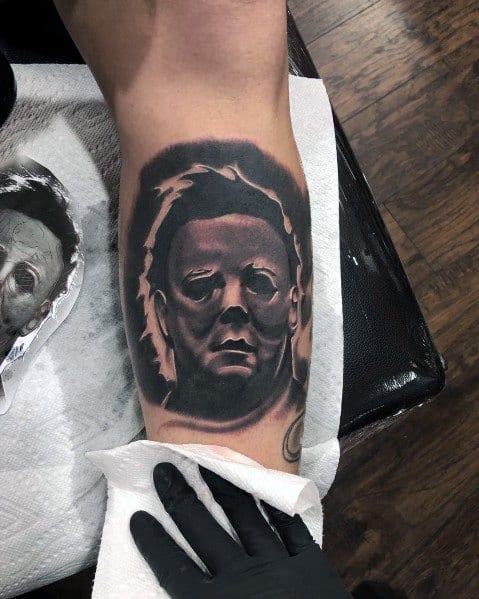 Bold black and gray Michael Myers tattoo, featuring his menacing mask with deep shadows for a dark and intense horror aesthetic.
