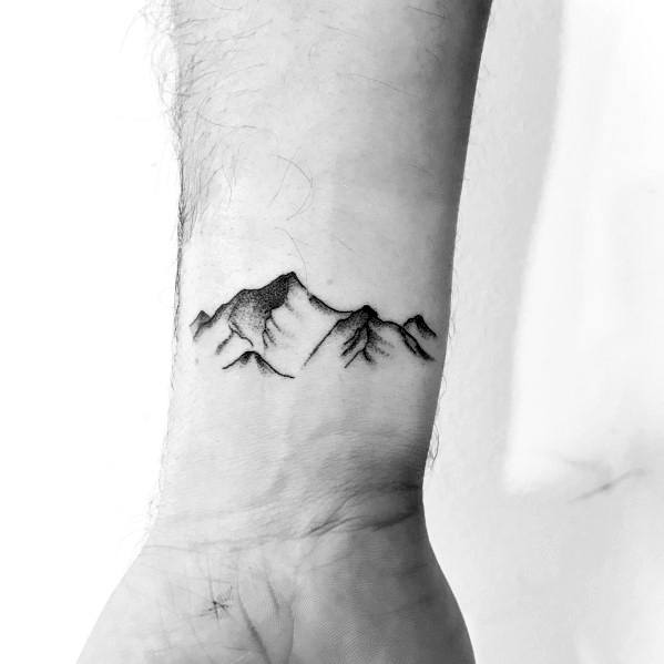 Minimalist mountain tattoo on the wrist, featuring fine lines and subtle shading for a delicate yet bold nature-inspired design.