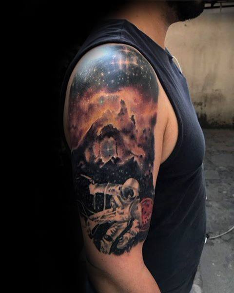 Tattoo of an astronaut amidst a nebula landscape on a man’s upper arm