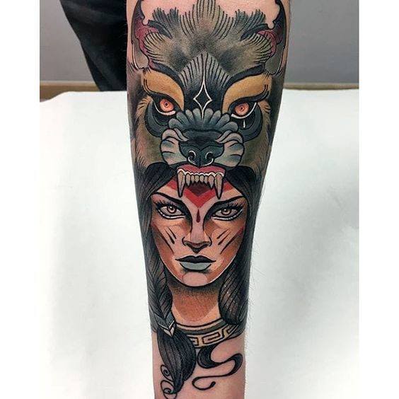 Neo-traditional tattoo of a fierce woman wearing a snarling wolf headdress, detailed shading, tribal markings, and bold ornamental accents.