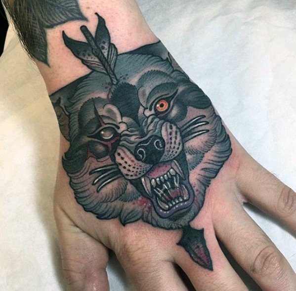 Neo-traditional hand tattoo of a snarling wolf with intense shading, one red eye, an arrow piercing its head, and bold black and grey details.