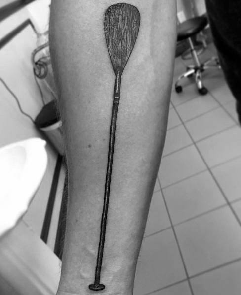 Detailed paddle tattoo on the forearm with a long handle and wood grain texture, symbolizing resilience, adventure, and a connection to water.