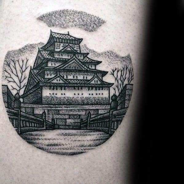 Dotwork-style tattoo of a traditional Japanese castle with a bridge, bare trees, and clouds, framed in a circular composition.