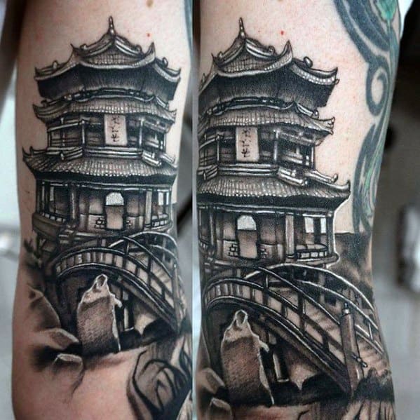 Realistic black and grey tattoo of a Japanese pagoda with an arched bridge and stone lantern, placed on the forearm.