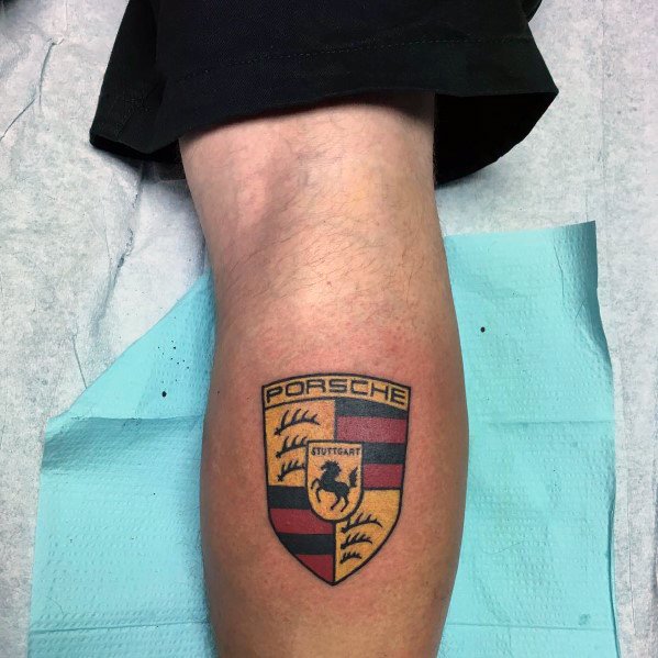 Vibrant Porsche emblem tattoo on the calf, featuring precise black, red, and gold colors.
