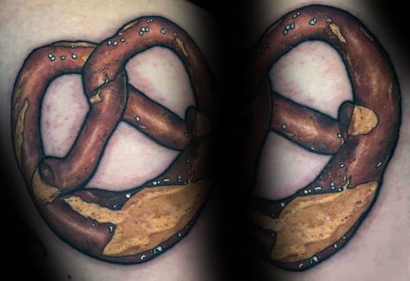 Realistic pretzel tattoo with rich brown shading, salt details, and golden highlights, creating a textured and three-dimensional effect.