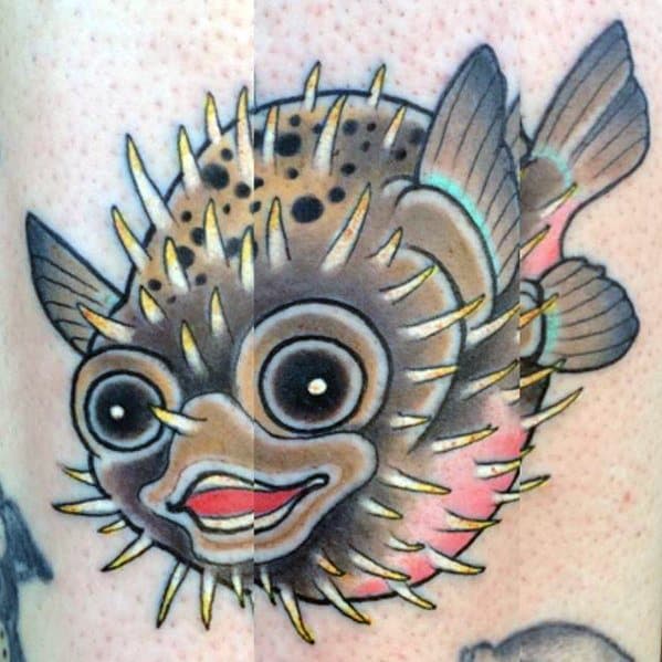 Colorful pufferfish tattoo with expressive eyes, sharp golden spines, and bold shading, giving it a playful and lively appearance.