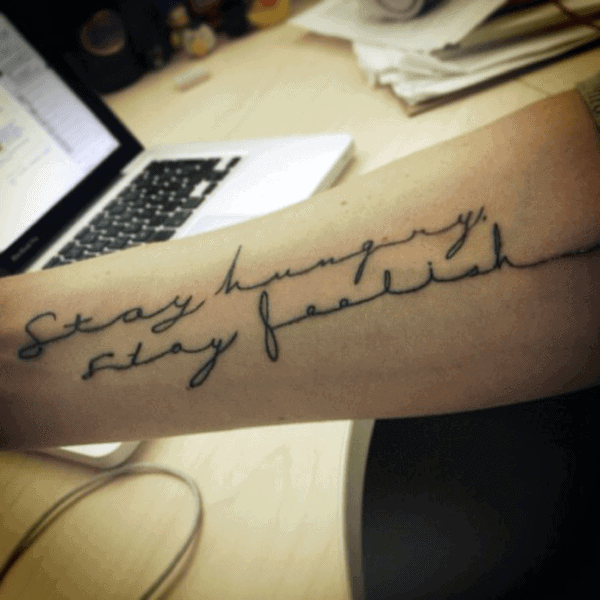 Forearm tattoo that reads "Stay hungry, stay foolish" in cursive script