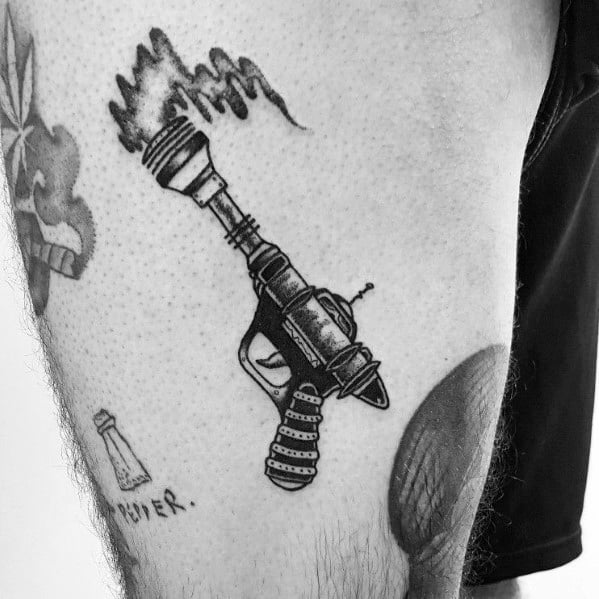 Black and grey ray gun tattoo with a retro sci-fi design, featuring bold linework, intricate shading, and an electric energy beam effect.