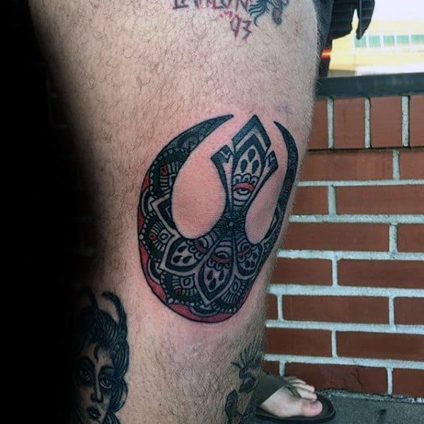 Tribal-style black and red Rebel Alliance tattoo on the side of a lower leg, featuring intricate geometric patterns.