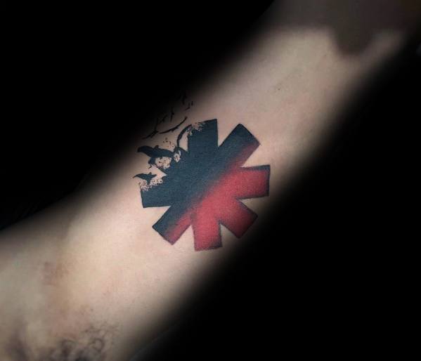 Forearm tattoo featuring the Red Hot Chili Peppers logo with a silhouette of a jumping figure and abstract shading for a bold artistic look.