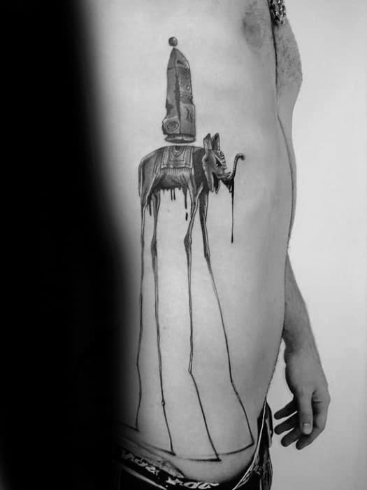 Black and grey Salvador Dali-style tattoo on the ribs featuring a surreal elephant with elongated legs and an obelisk dripping with detail.