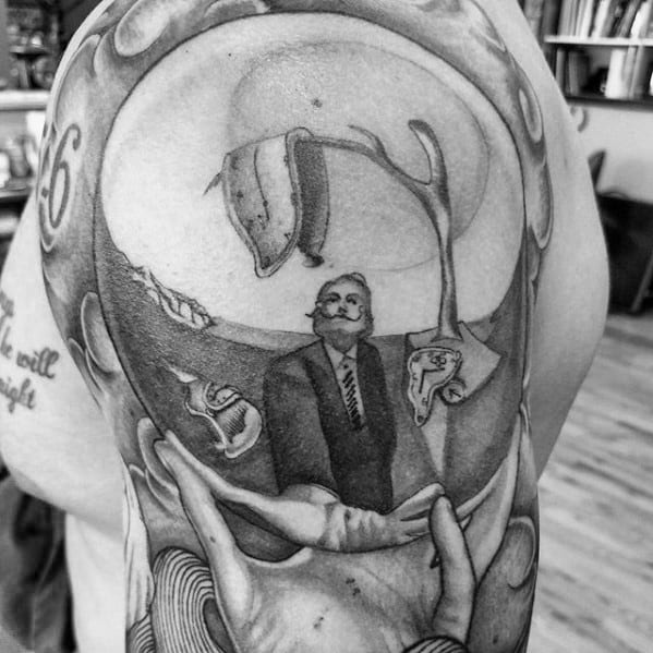 Surreal Salvador Dali shoulder tattoo in black and grey featuring melting clocks, abstract limbs, and Dali in a suit within a distorted dreamscape.