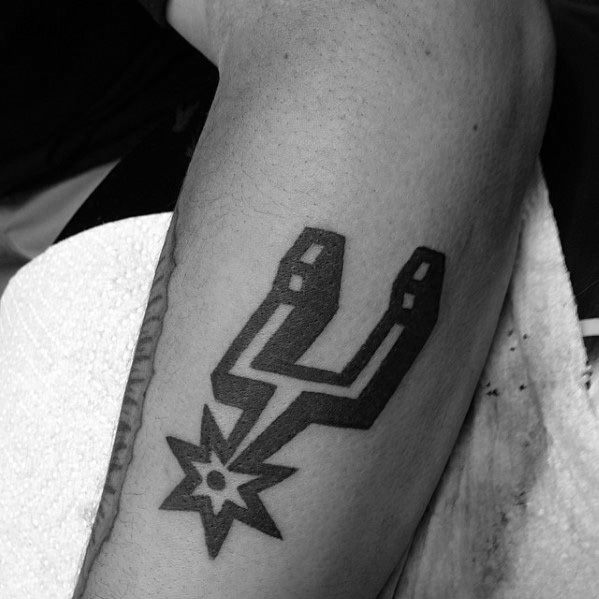 Bold black San Antonio Spurs logo tattoo on the leg, featuring the iconic spur design with clean, sharp lines and solid shading.