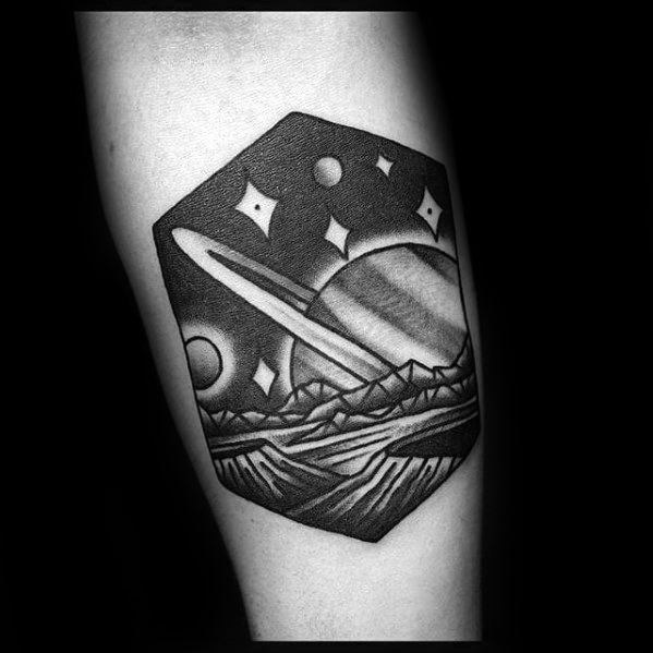 Geometric Saturn tattoo design for men showing a ringed planet above alien mountains and stars in black and grey shading.