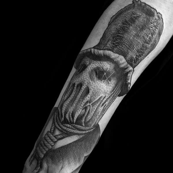 Black and grey scarecrow tattoo with a stitched burlap sack mask, hollow eyes, tall hat, and thick rope around the neck.