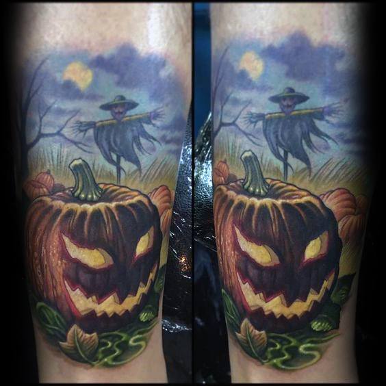 Colorful scarecrow tattoo with a glowing-eyed jack-o'-lantern in the foreground and eerie scarecrow in a moonlit field behind.