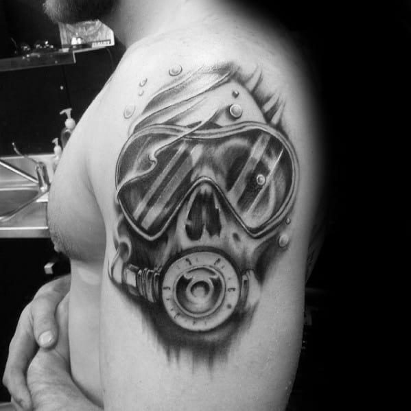 Realistic black and grey tattoo of a scuba diver mask on upper arm, with a skull reflection inside the goggles.