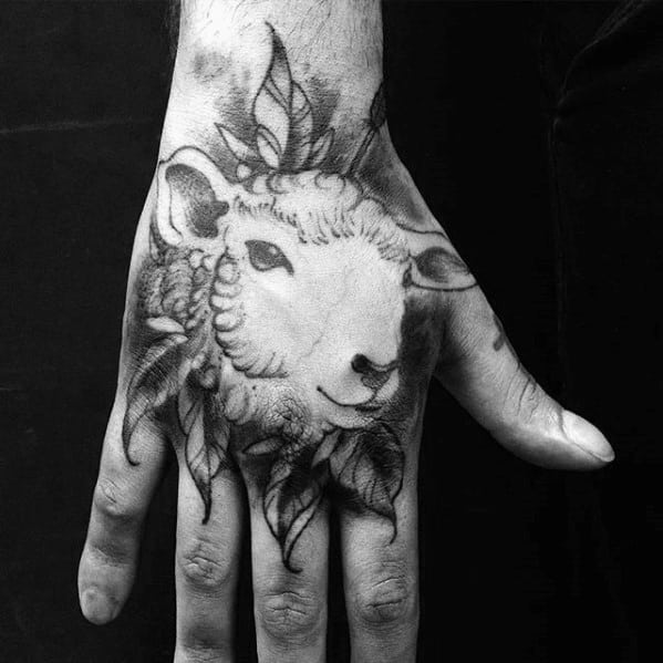 Hand with a detailed black ink tattoo of a sheep's head with leaves around it