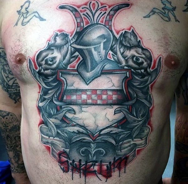 Bold chest tattoo of a medieval coat of arms with a knight’s helmet, two lions, red checkered shield, and the name “SHAUN” in stylized lettering.