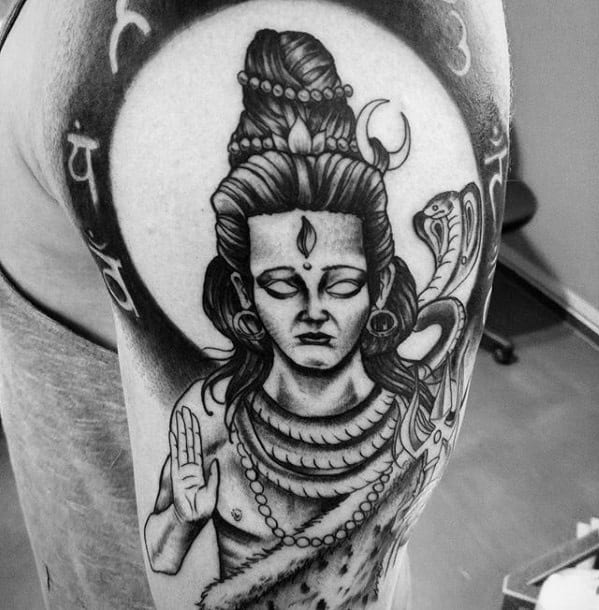 Upper arm tattoo of Lord Shiva with closed eyes, a calm expression, snake around the neck, and Sanskrit script forming a halo behind him.