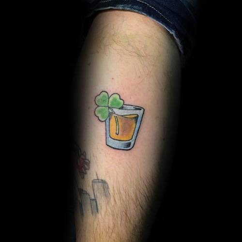 Minimalist shot glass tattoo with a golden drink and a green four-leaf clover, symbolizing luck and celebration in a simple design.