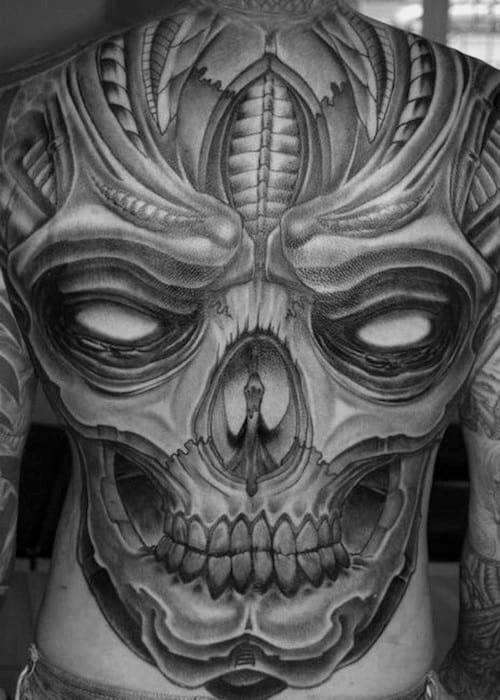 Futuristic biomechanical skull back tattoo with bold shading, layered textures, and a haunting figure within the nasal cavity.