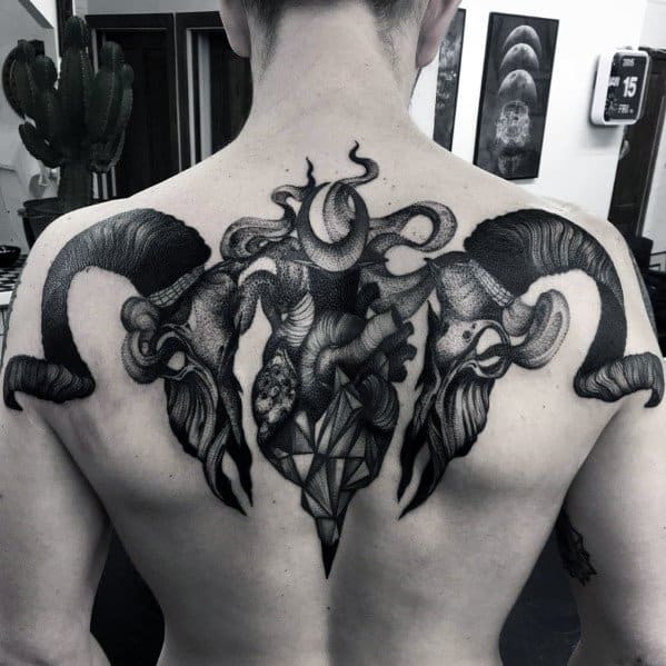 Dark surreal back tattoo with twisted ram skulls, anatomical heart, and tentacles forming a symmetrical, abstract composition.