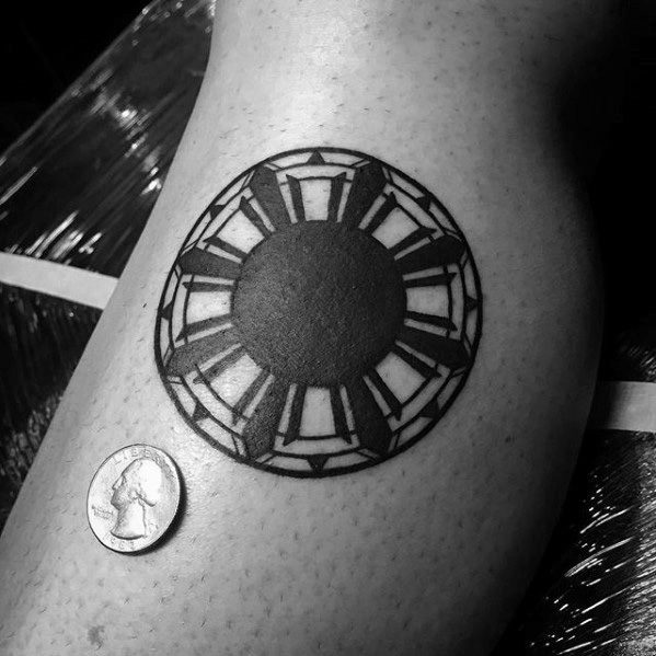 Small Filipino sun tattoo on the leg with bold black rays and a solid circular center, shown next to a coin for size reference.