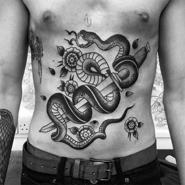 Black and grey snake and dagger tattoo across the stomach, featuring bold shading, floral details, and a fierce traditional design.