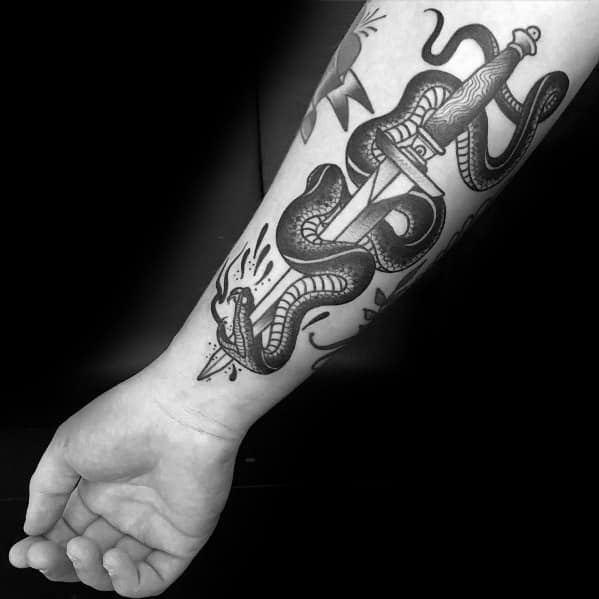 Black and grey snake and dagger tattoo on forearm, featuring bold lines, detailed shading, and a striking traditional design.