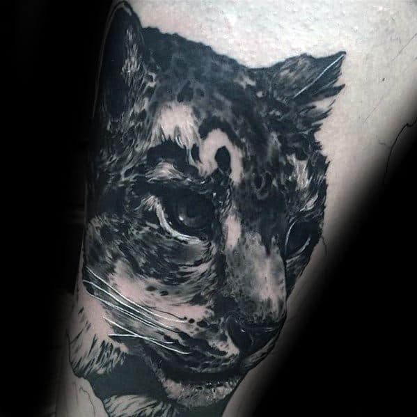 Black and gray snow leopard tattoo with a shadowy, textured look, capturing the feline’s intense gaze and mysterious presence.