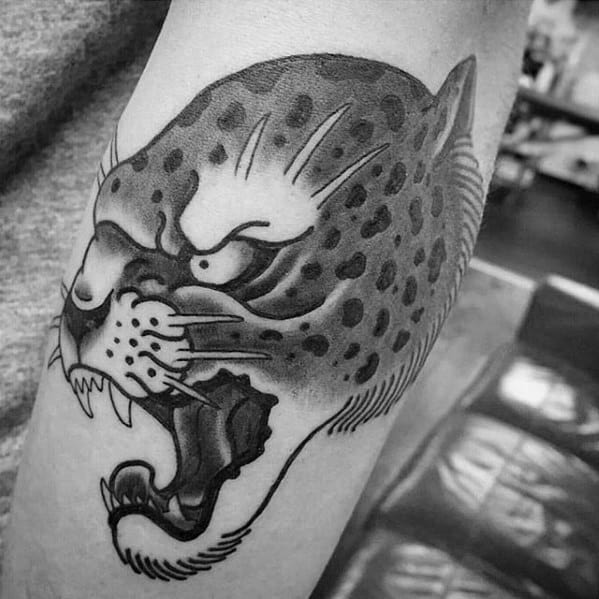 Traditional-style snow leopard tattoo in blackwork, featuring bold lines, fierce expression, and vintage shading on the bicep.