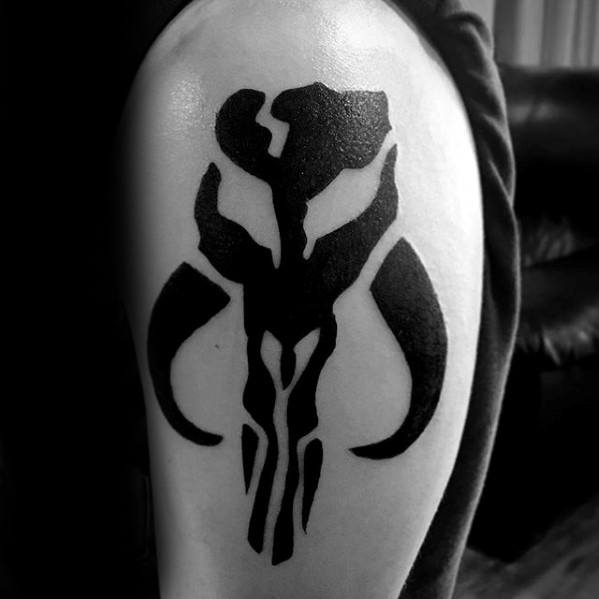 Bold black Mythosaur skull tattoo on the upper arm, featuring clean lines and a powerful Mandalorian symbol silhouette.