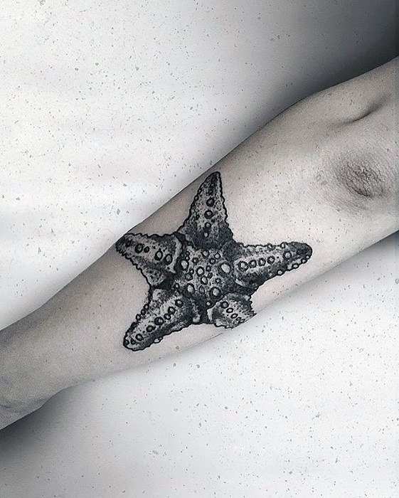 Highly detailed black and grey starfish tattoo on the forearm, featuring realistic texture and strong dotwork shading.