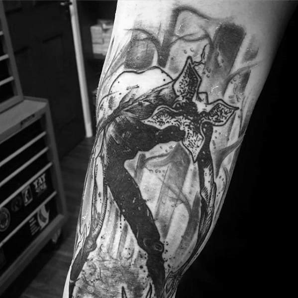 Black and grey tattoo of the Demogorgon from Stranger Things emerging from a forest scene, with eerie and intense shading details.