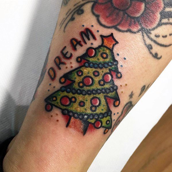 Traditional Christmas tree tattoo with bold outlines, red ornaments, string lights, and a star on top, featuring the word "DREAM" in stylized text.