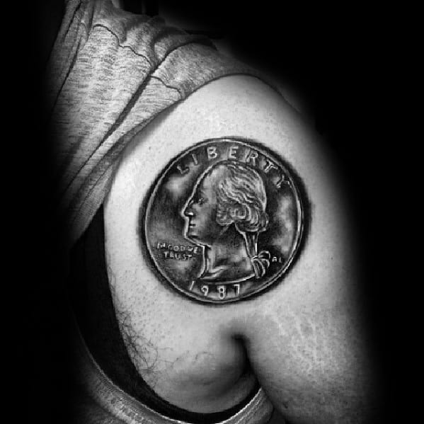 Realistic tattoo of a 1987 Washington quarter on the upper arm, featuring detailed shading for a three-dimensional coin effect.