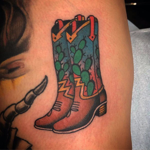 Tattoo of a pair of cowboy boots with a cactus pattern, combining Western style with bold, colorful design elements for a unique look.