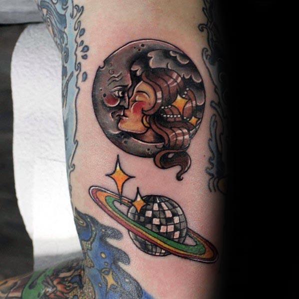 Creative tattoo featuring a disco ball planet with rings and a moon with a woman's face, blending celestial and retro themes in bold colors.
